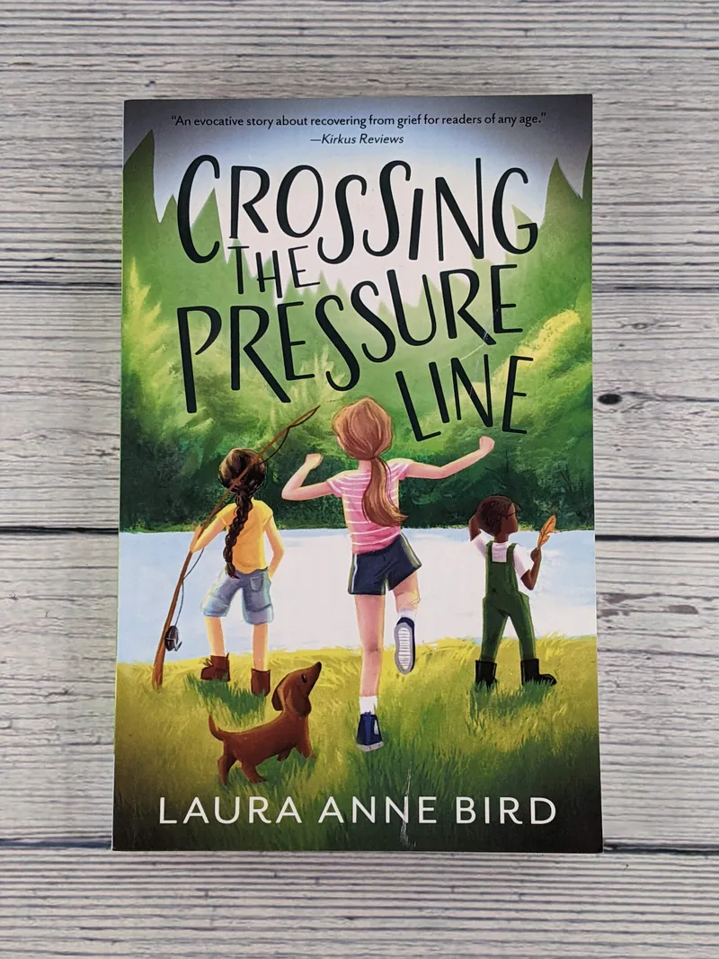 A paperback fiction book for tweens with an image of three children fishing with their dog, titled Crossing the Pressure Line by Laura Anne Bird.
