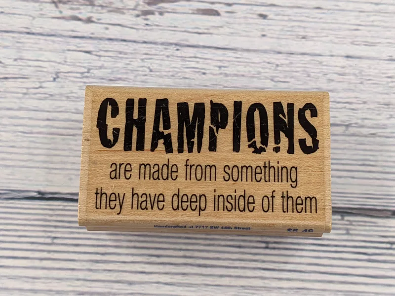A wood mounted rubber stamp with the words "Champions are made from something they have deep inside of them."