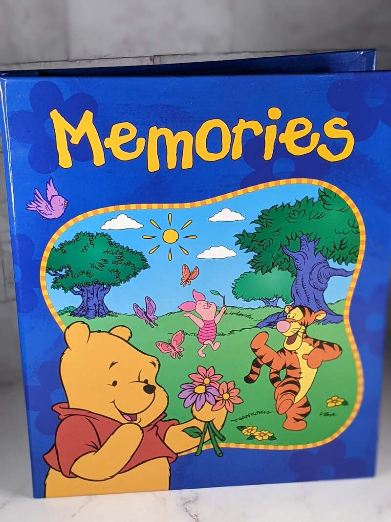 A blue scrapbook photo album with the word "memories" on the cover and images of Winnie the Pooh, Piglet and Tigger.