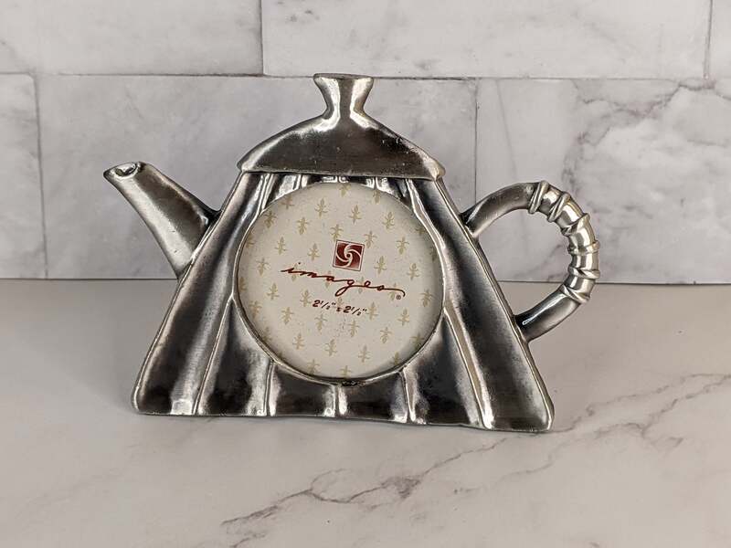 A silver metal photo frame shaped like a teapot.