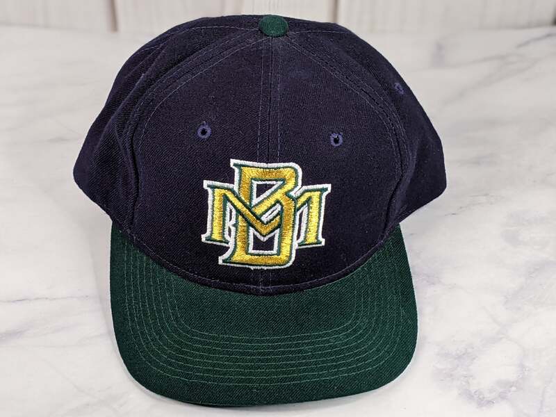 A navy blue baseball cap with a green bill and a vintage gold embroidered MB logo of the Milwaukee Brewers.