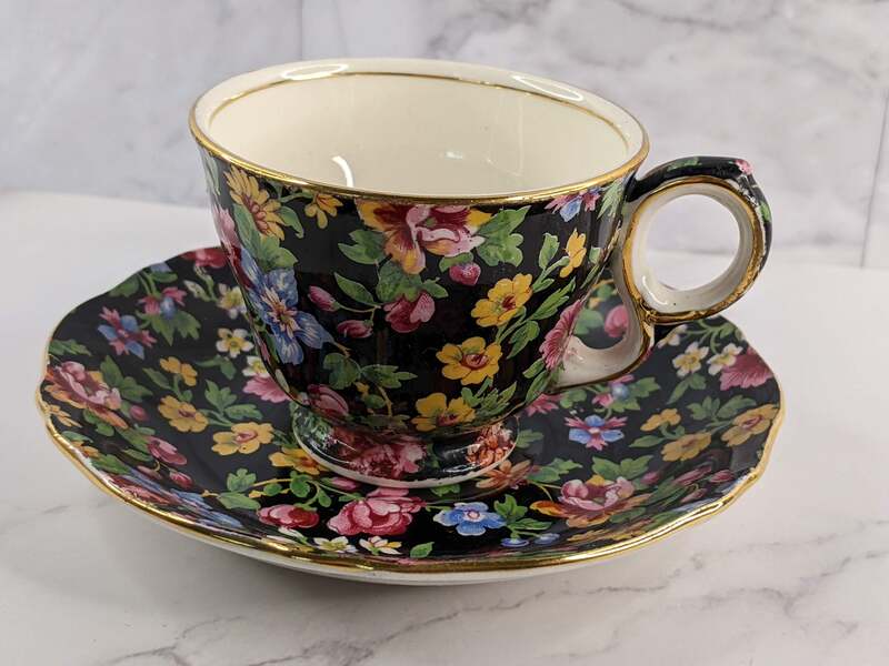 A teacup and saucer that is black on the outside with a pink and blue flower pattern.